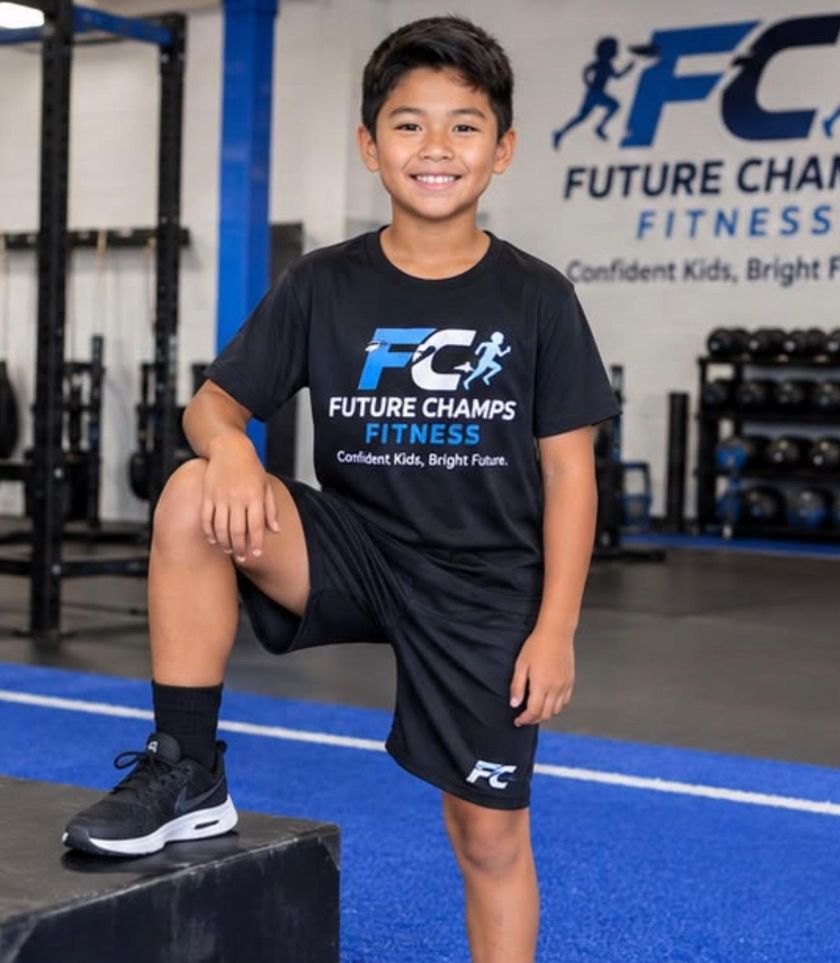 A boy in a Future Champs Fitness shirt resting one foot on a plyo box